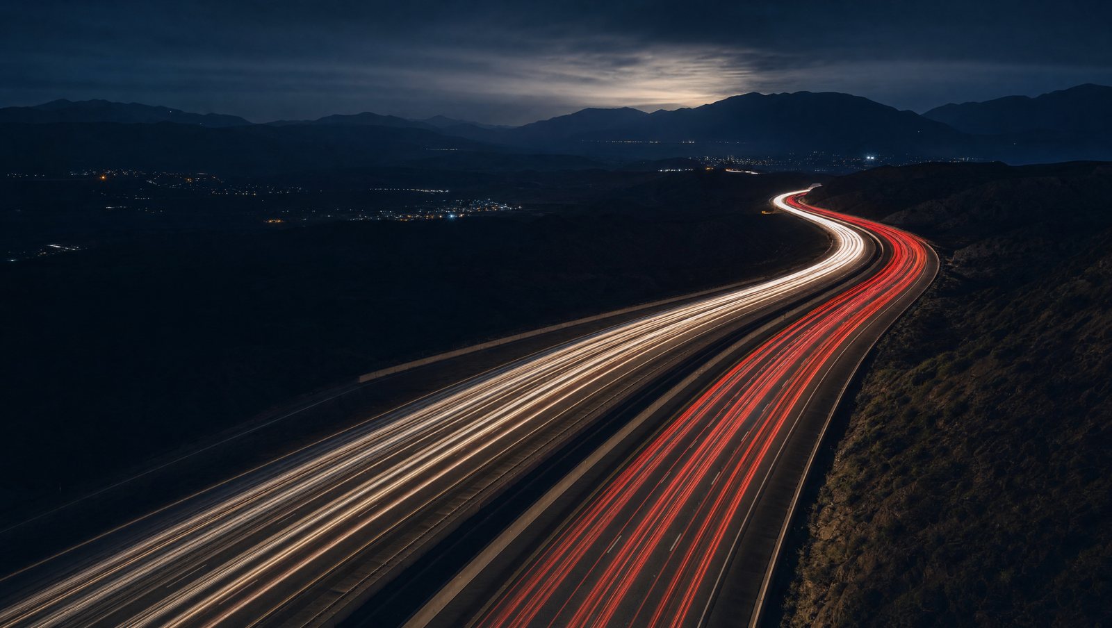Long-exposure light trails of traffic on a winding highway at night